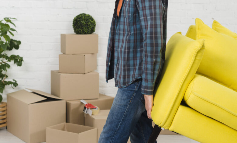 smiling-portrait-young-man-lifting-yellow-sofa-new-house - مرينا لتجارة اثاث مستعمل